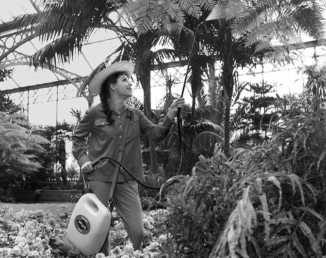 Altes Schwarz-Weiß-Bild mit Frau, die in Gewächshaus Pflanzenschutzmittel versprüht